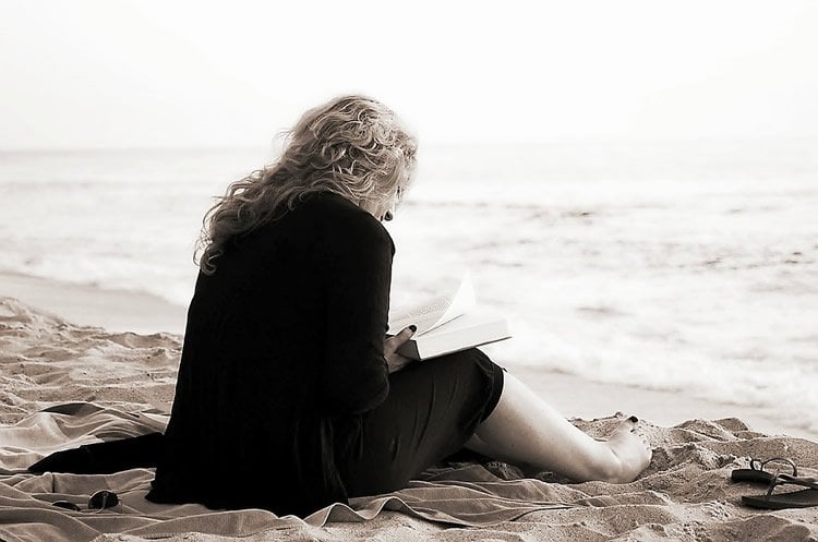 Image shows a woman reading on a beach.