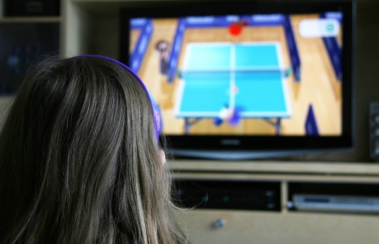 Image shows a child playing a tennis video game.