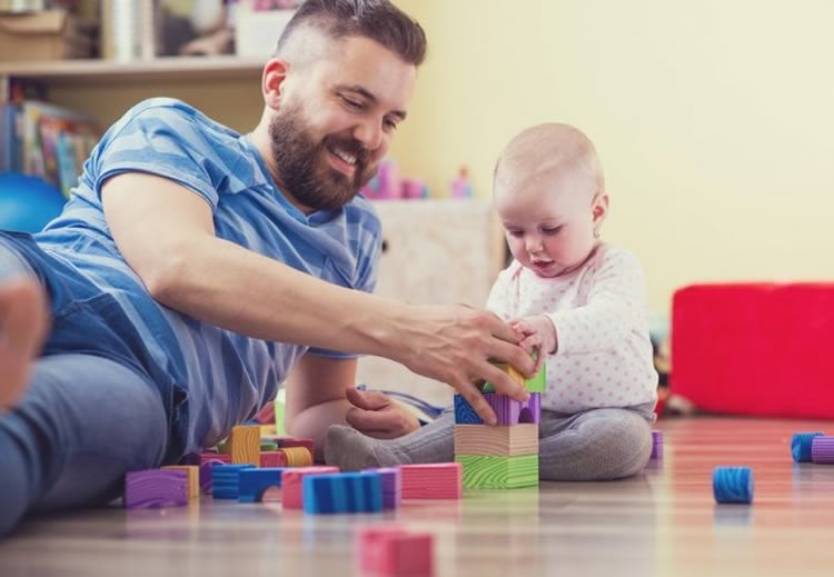 Image shows a dad playing blocks with a small baby.