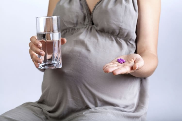 Image shows a pregnant woman holding folic acid pills.