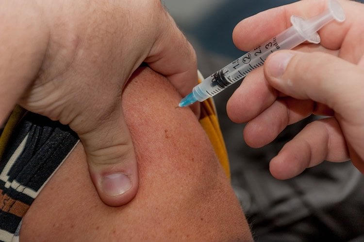 Image shows a person getting a vaccination.
