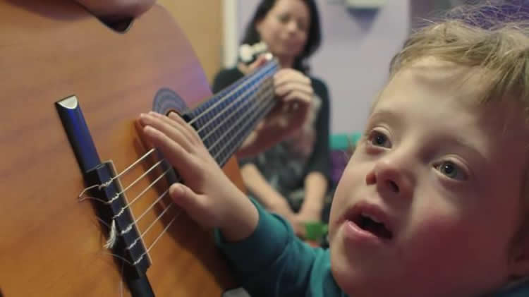 Image shows a little boy playing a guitar.