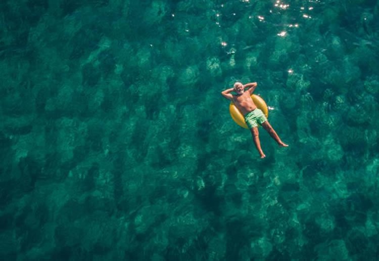 Image shows a man relaxing on a floatie in the ocean.