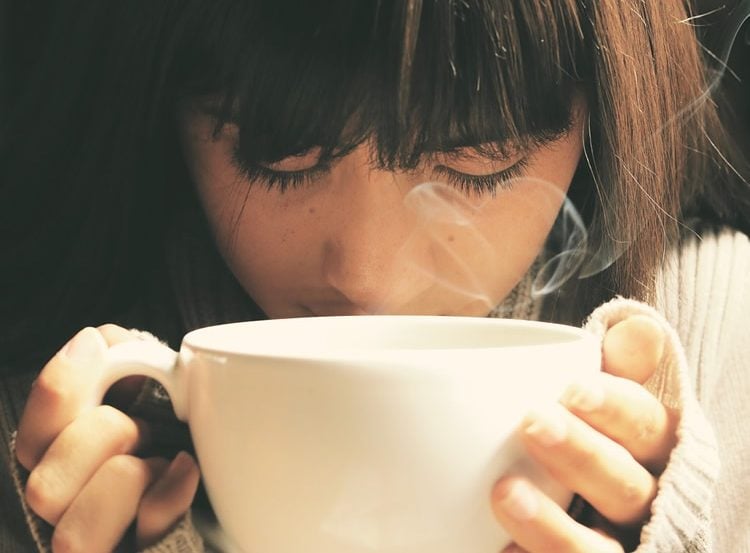 Image shows a woman drinking coffee.