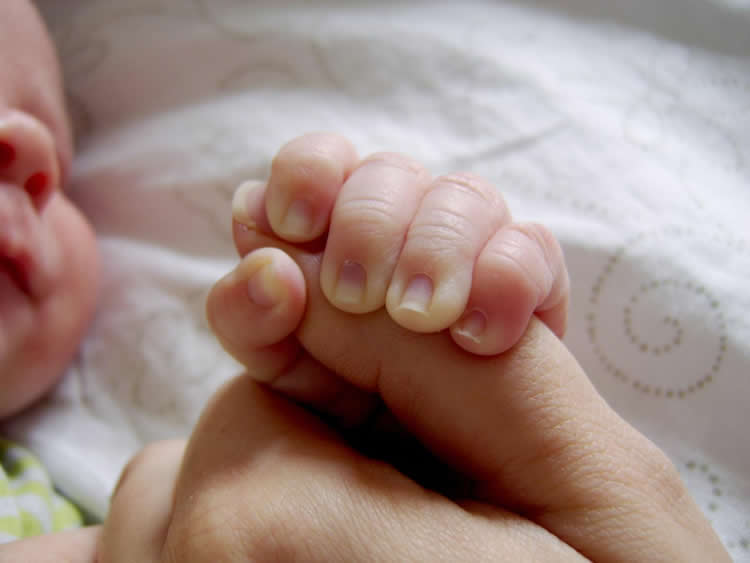 This image shows a baby holding its parent's thumb.