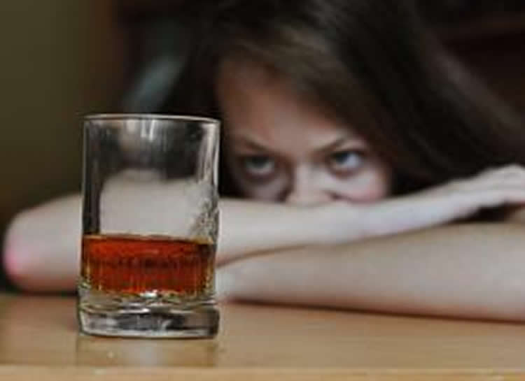 Image shows a woman looking at a drink of whiskey.