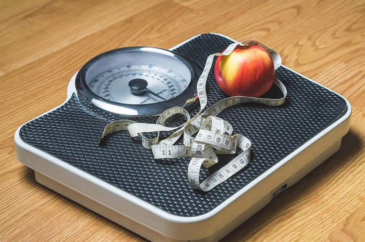 Image shows a scale, tape measure and apple.