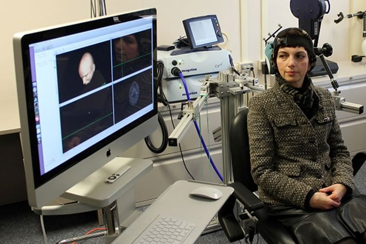 Image shows a lady sitting next to a monitor undergoing rTMS.