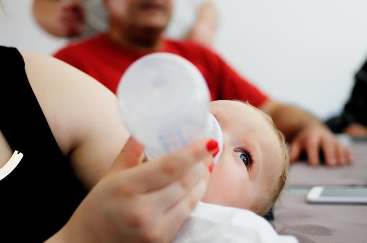 Image shows a baby drinking from a bottle.