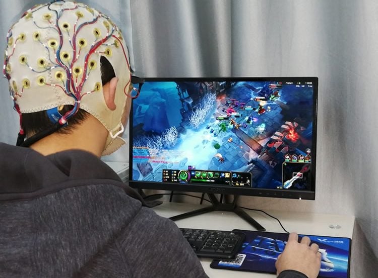 Image shows a person wearing an EEG cap playing a computer game.