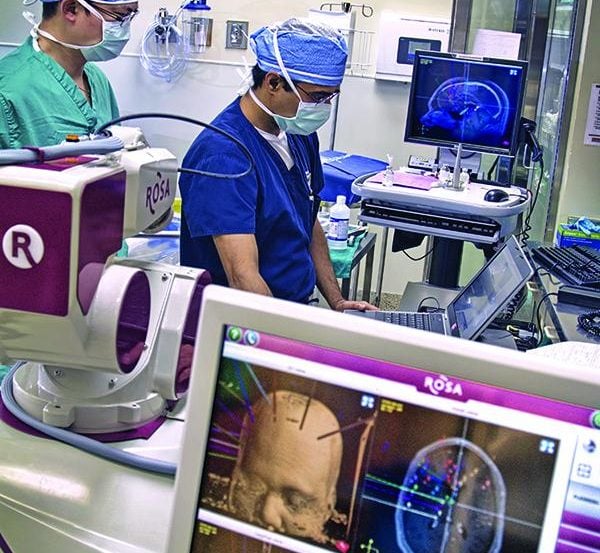 Two surgeons are shown in an operating room with a monitor in the foreground.