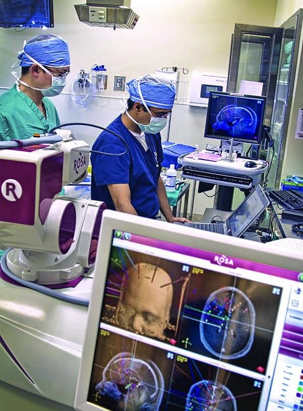 Two surgeons are shown in an operating room with a monitor in the foreground.
