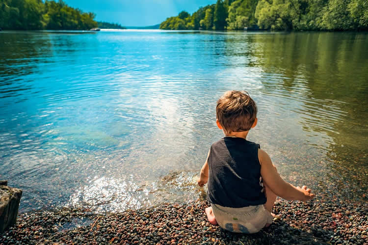 This shows a child sitting by a beautiful lake