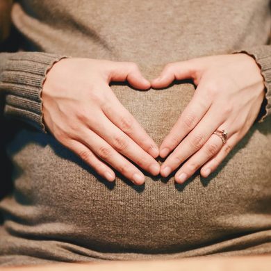 This shows a pregnant woman making a heart shape with her hands over her belly