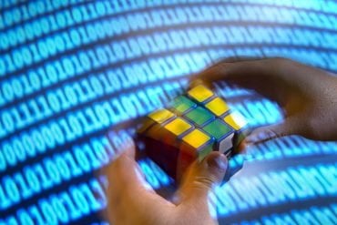 This shows a binary screen and a person solving the rubiks cube