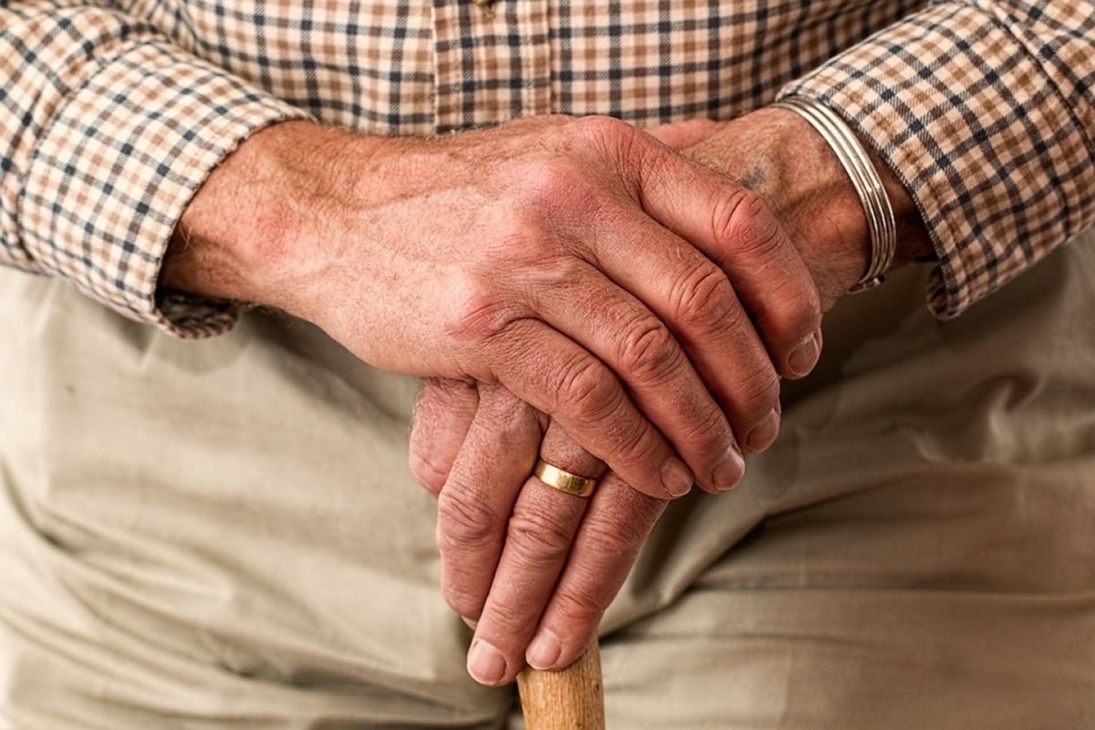This shows an old man's hands holding a walking stick
