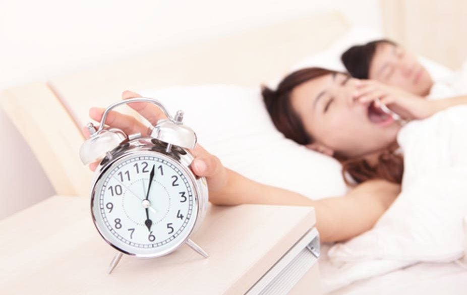 This shows a sleepy woman reaching for an alarm clock