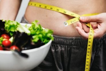 This shows a woman next to a bowl of salad measuring her tummy