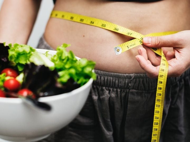 This shows a woman next to a bowl of salad measuring her tummy