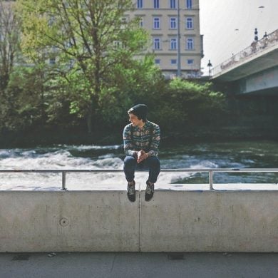 This shows a teen boy sitting on a bridge