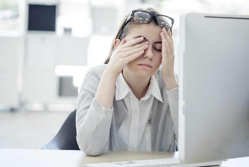 This shows a woman sitting at her desk, rubbing her eyes