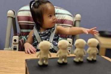 This shows a toddler with four dolls in front of her
