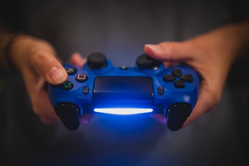 This shows a pair of hands holding a blue PS4 controller