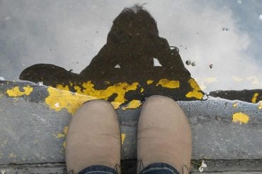 This shows a person's shoes and reflection in a puddle