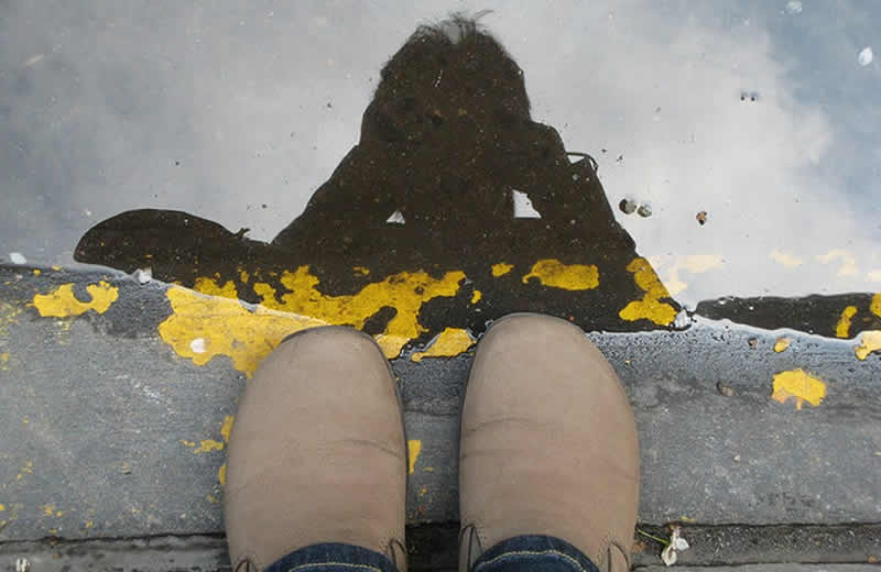 This shows a person's shoes and reflection in a puddle