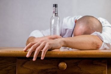 This shows a person laying with their head on the table and an empty alcohol bottle