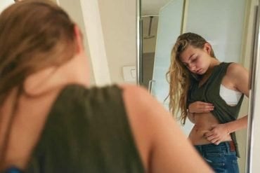 This shows an underweight teenager looking at her stomach in the mirror