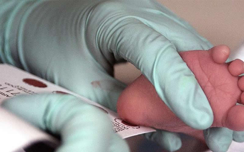This shows a doctor giving a newborn a blood prick test