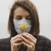 This shows a woman in a facemask smelling a flower