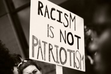 This shows a person holding a sign that reads racism is not patriotism