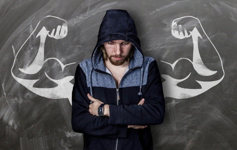 This shows a man with folded arms and a drawing of muscular arms behind him