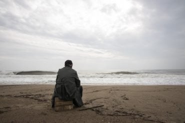 This shows a man sitting alone on a beach