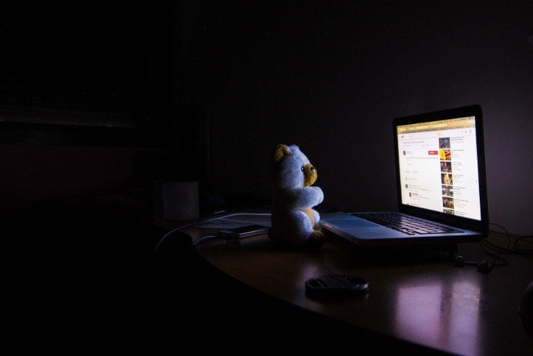 This shows a teddybear sitting at a computer at night