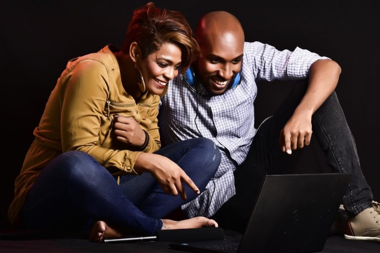 The image shows two young adults laughing while looking at a computer monitor