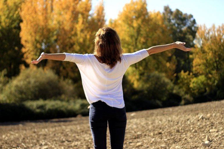 This shows a woman with her arms outstretched in a beautiful field