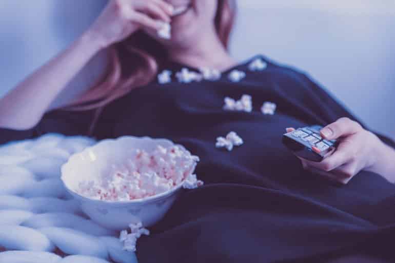 This shows a woman with a TV remote in her hand, eating popcorn