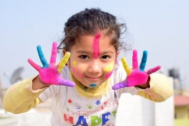 This shows a happy little girl with her hands painted up like a rainbow