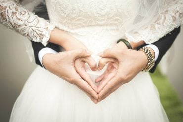 This shows a bride and groom making heart signs with their hands