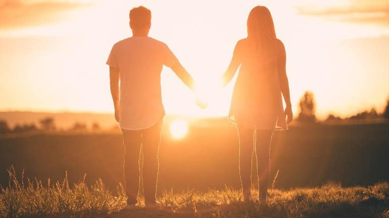 Esto muestra a una pareja tomados de la mano en la puesta de sol.