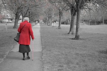 This shows an older lady walking in a park with a cane