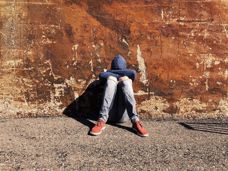 This shows a teenager huddled up against a wall