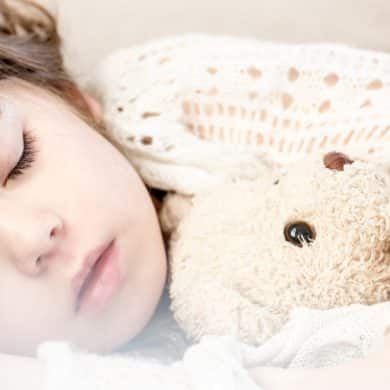 This shows a little girl sleeping with her teddy bear