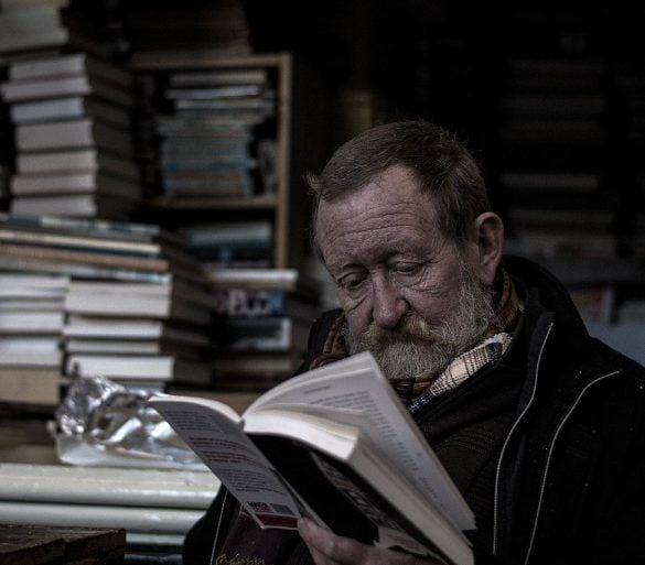This shows an older man reading a book in a bookstore