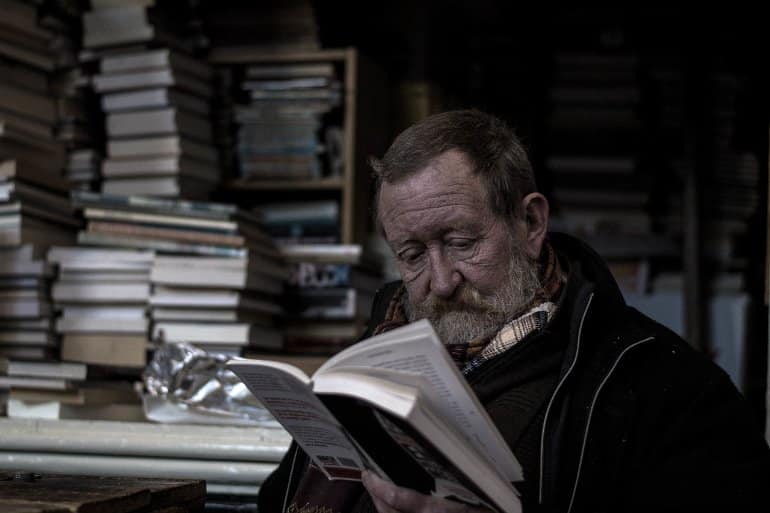 This shows an older man reading a book in a bookstore