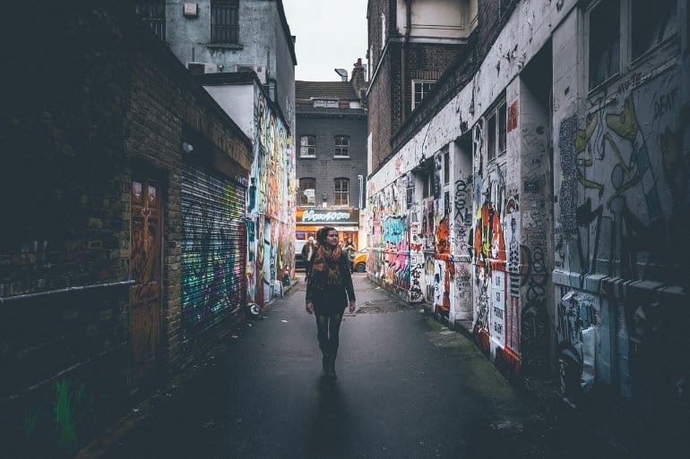 This shows a woman walking down a graffiti covered alleyway
