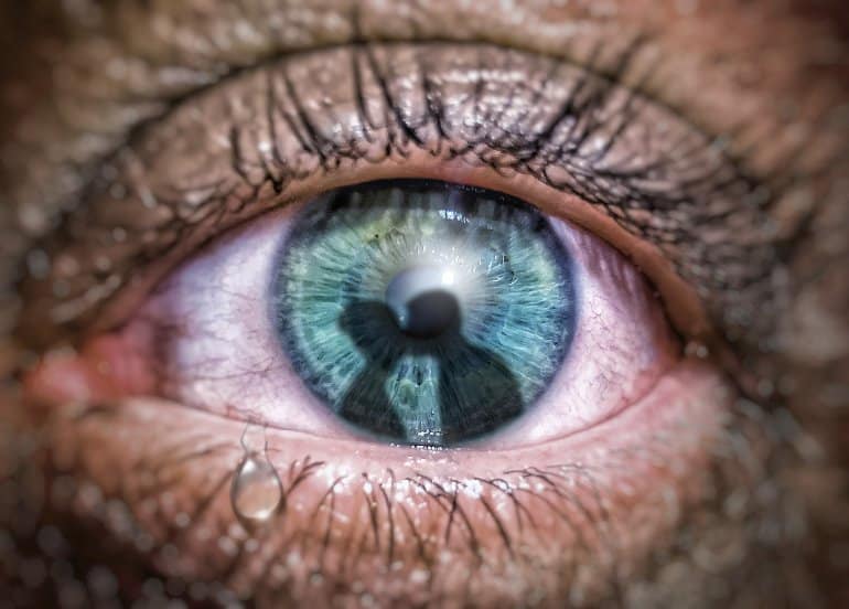 This shows a man's green eye with a reflection of two people kissing in it